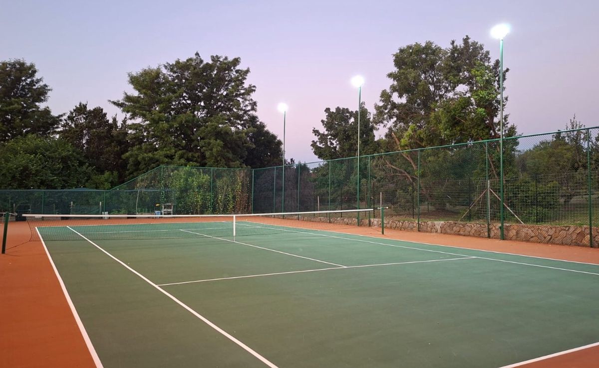 Tennis court at dusk showing NineCourts lighting masts positioned around the playing surface