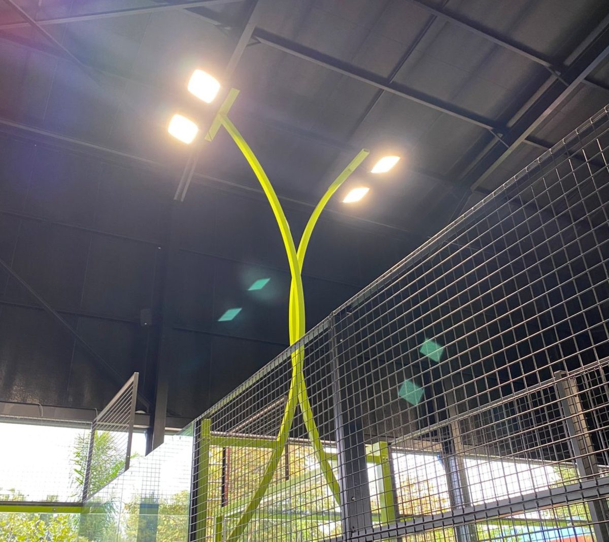 Distinctive yellow Y-shaped twin-lamp light fixture above a NineCourts padel court installation