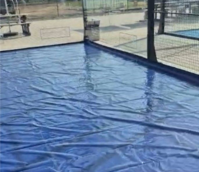 Blue PVC weather protection cover laid across a NineCourts padel court to keep the playing surface dry during rainfall
