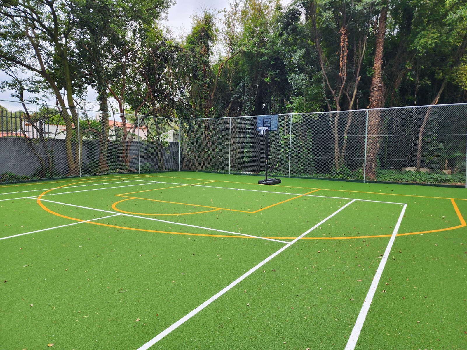Sandhurst finished Astro Turf court with chain link perimeter fencing and basketball hoop, set within a wooded private garden