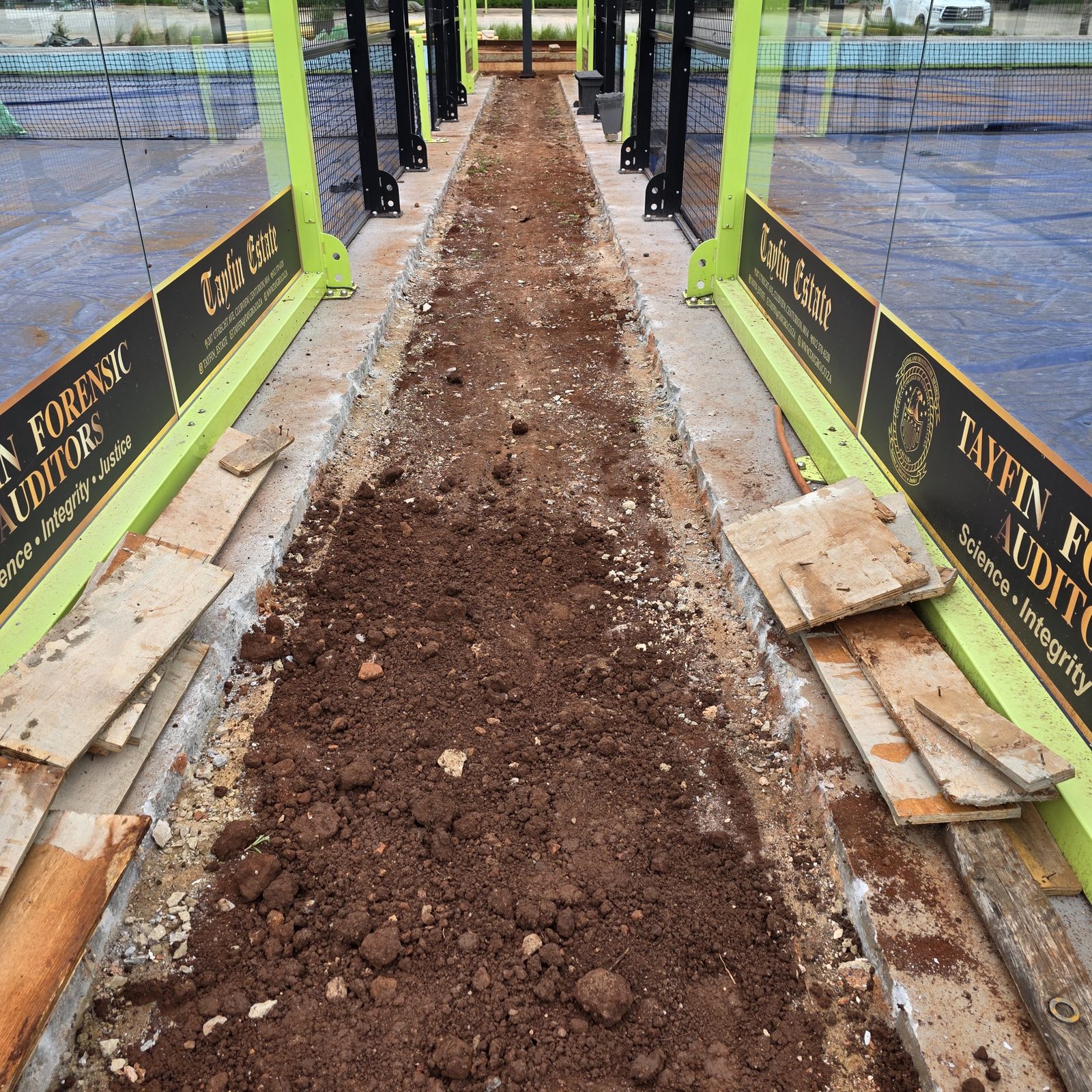 Tayfin Country Club court perimeter under preparation — exposed base, levelled ground, and timber boards in place ahead of the new surface installation